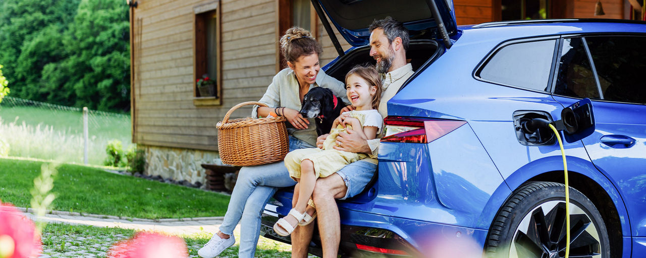 Familie mit Hund sitzt im Kofferraum eines Autos vor einem Haus