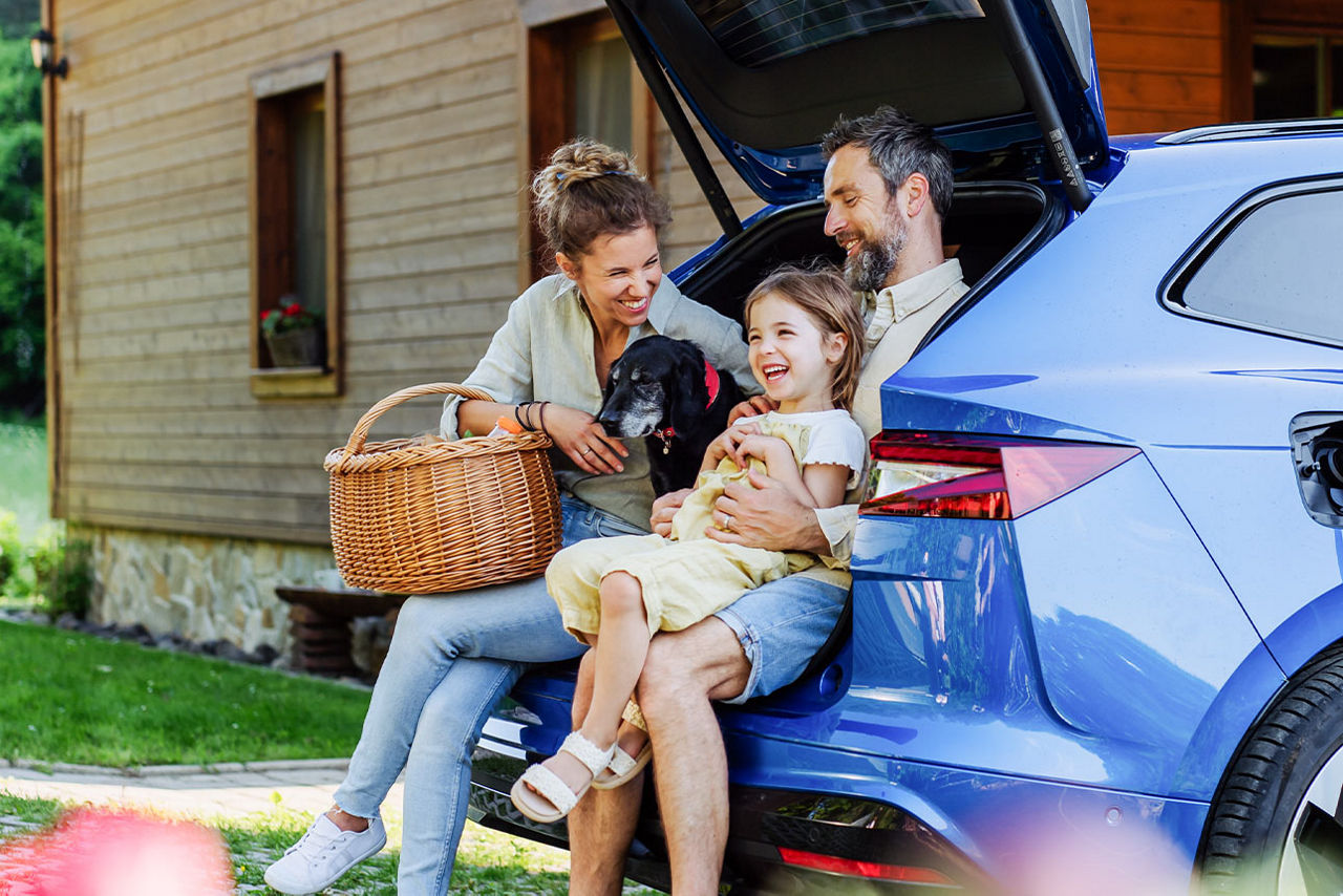 Familie mit Hund sitzt im Kofferraum eines Autos vor einem Haus