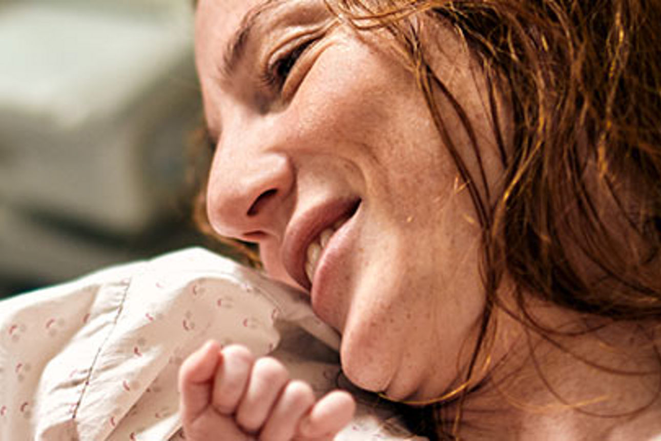 Eine fröhliche Frau lächelt warm, während sie ihr Baby in den Armen hält und einen Moment der Liebe und des Glücks zeigt.