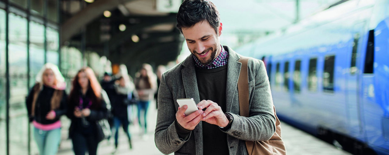 Mann am Bahngleis mit Handy in der Hand