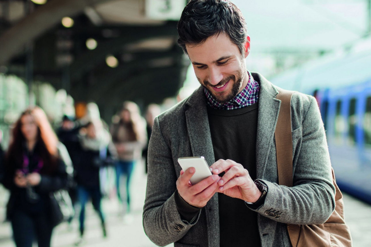 Mann am Bahngleis mit Handy in der Hand