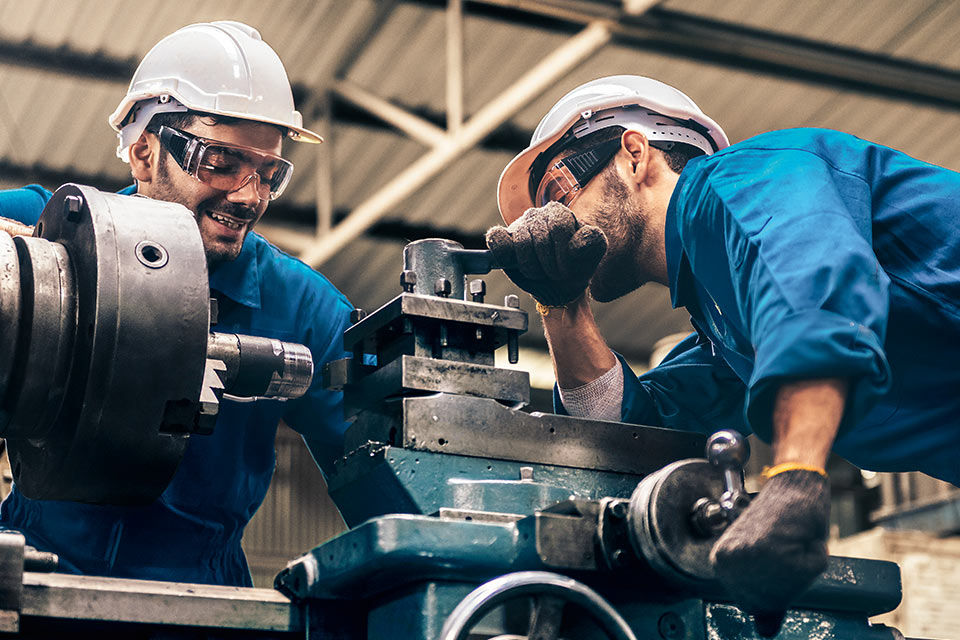 Zwei Männer mit Helm und Schutzbrille arbeiten an einer Maschine