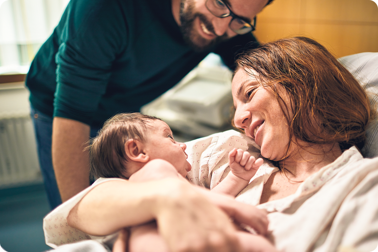 Eine Frau hält ihr neugeborenes Baby im Arm und freut sich gemeinsam mit dem Vater
