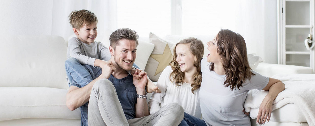 Junge Familie lacht miteinander im Wohnzimmer