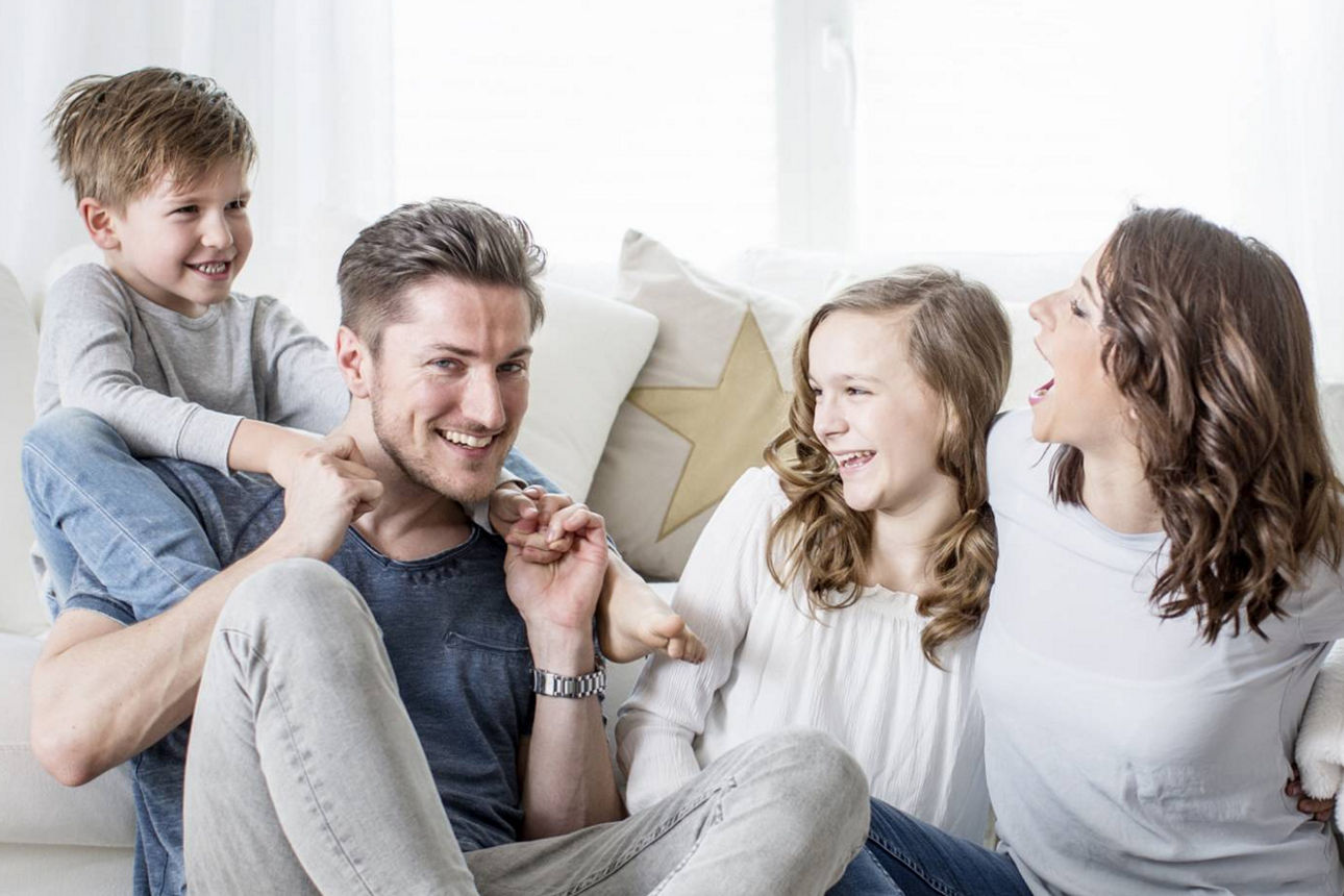 Junge Familie lacht miteinander im Wohnzimmer