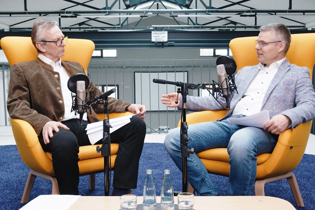 Zwei Personen im Gespräch vor Mikrofonen, Podcast- oder Interviewaufnahme in modernem Studio.