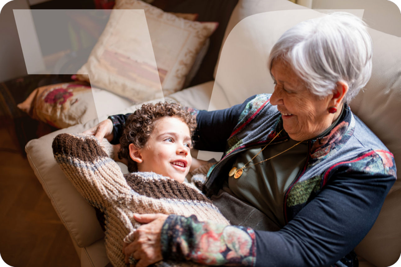 Großmutter hält ihr Enkelkind liebevoll auf dem Sofa im Arm.