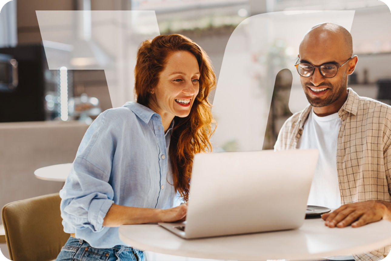 Zwei Arbeitskollegen sitzen gemeinsam an einem Tisch und arbeiten an einem Laptop in einer hellen, modernen Umgebung.