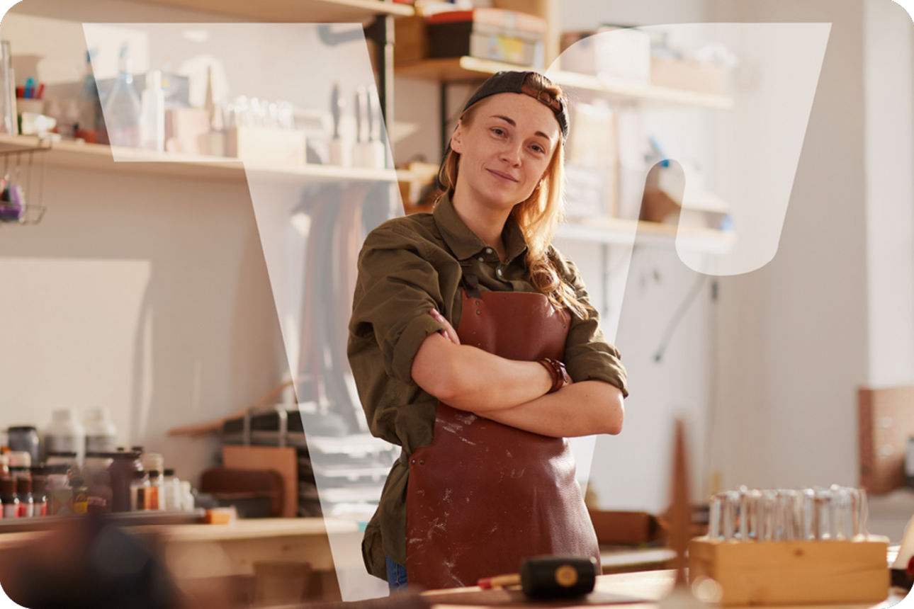 Frau in einer Werkstatt mit Lederschürze steht vor Werkbank und Werkzeugen