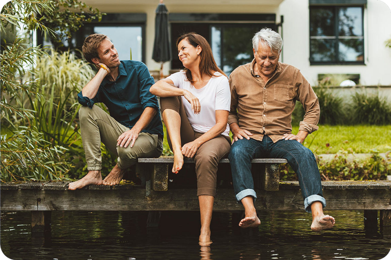 Eine Familie sitzt am Ufer im Garten ihres Hauses.