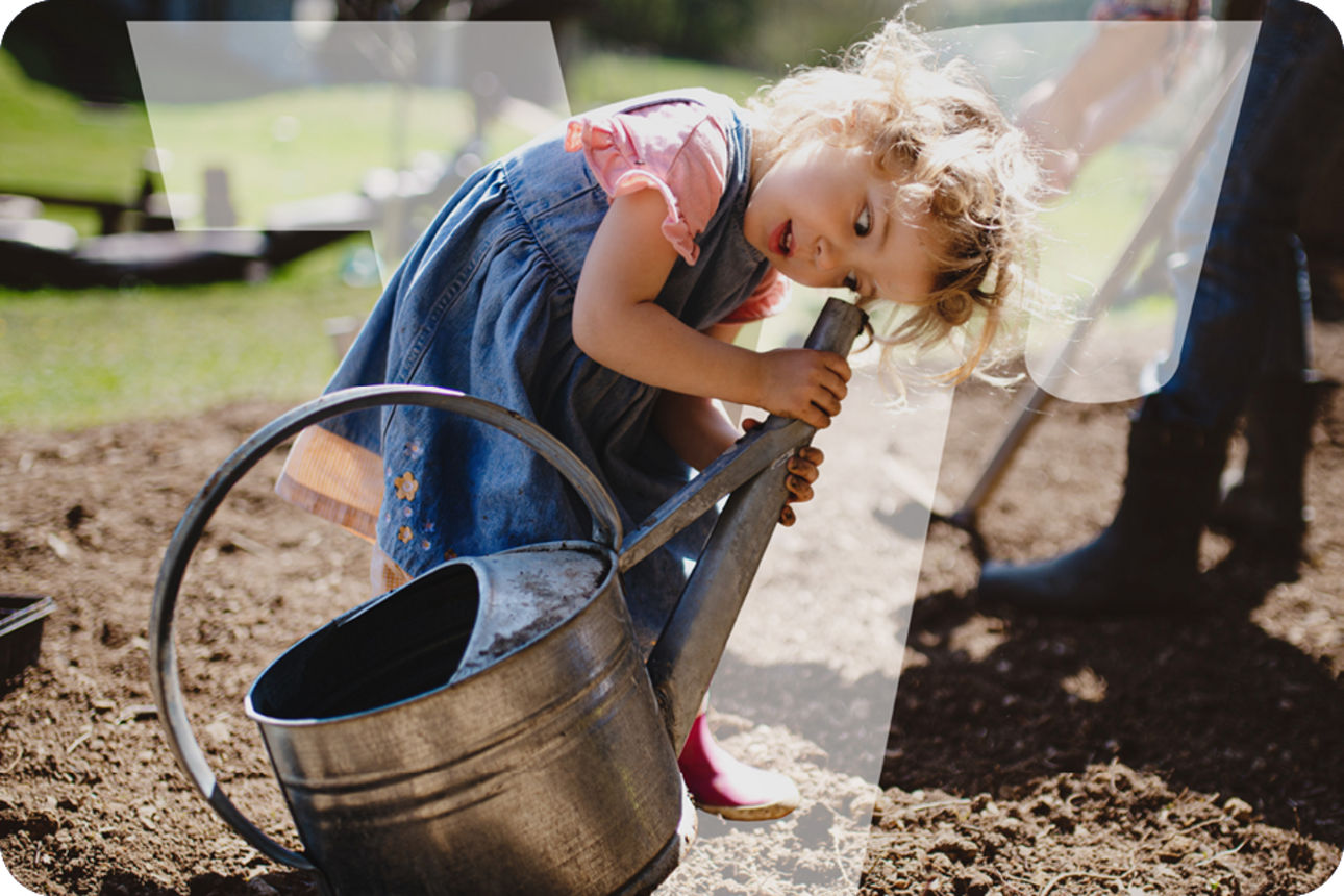 Kind gießt mit einer großen Metall-Gießkanne Erde im Garten