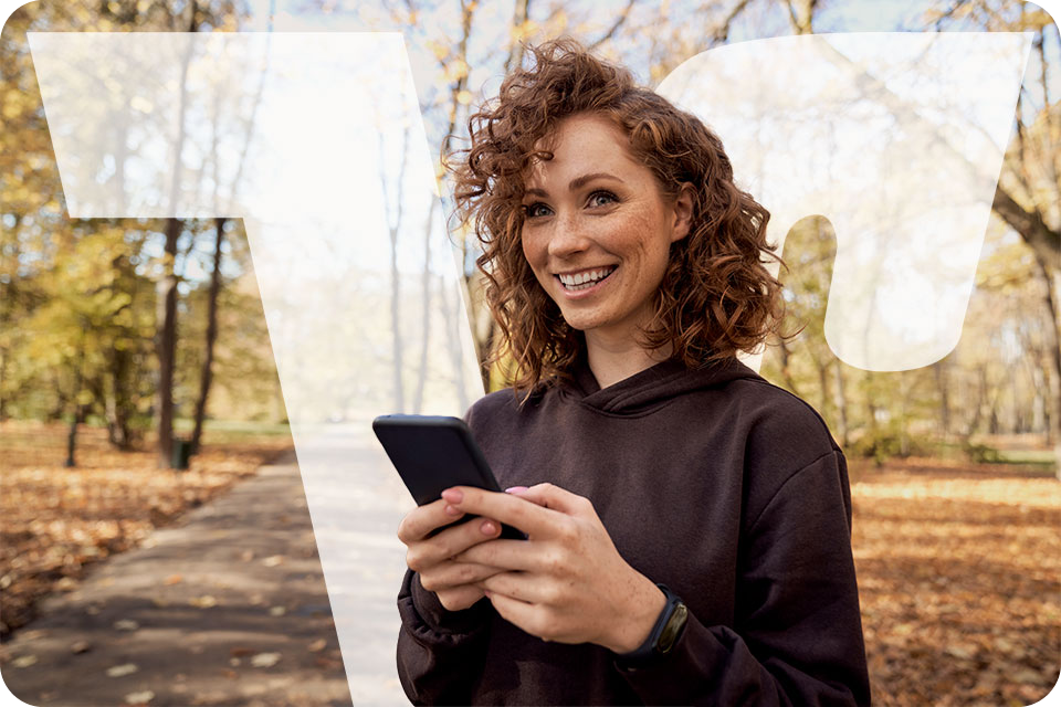 Frau mit lockigem Haar nutzt ein Smartphone in einem herbstlichen Park.