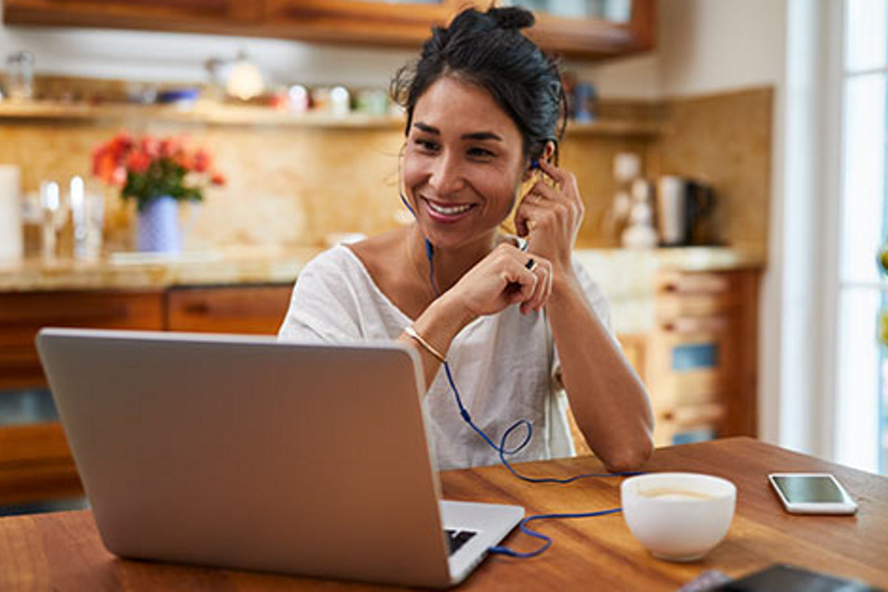 Eine lächelnde junge Frau telefoniert per Headset am Laptop