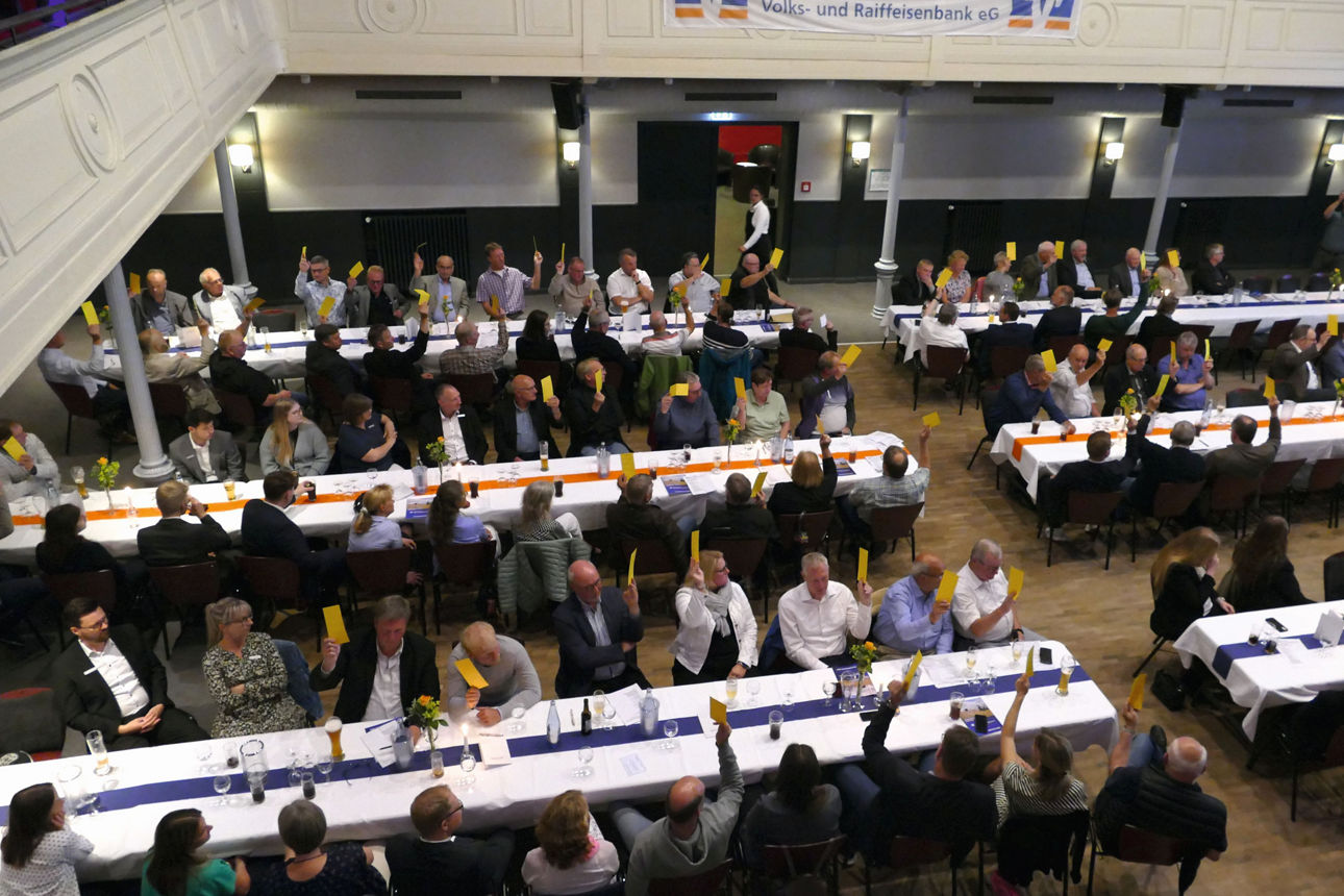 Menschen sitzen an Tischen im Heider Stadttheater und heben Stimmzettel