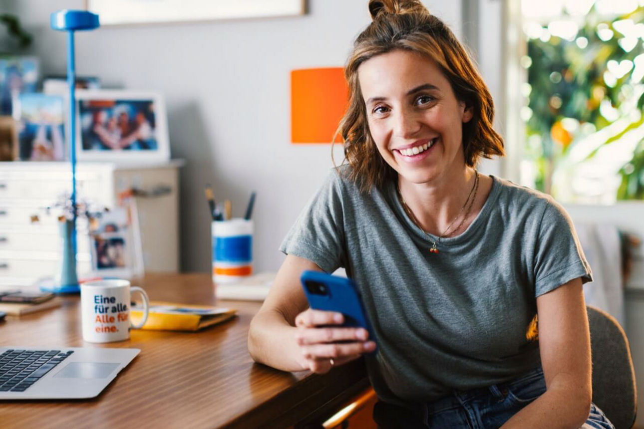 Junge Frau mit Smartphone am Schreibtisch