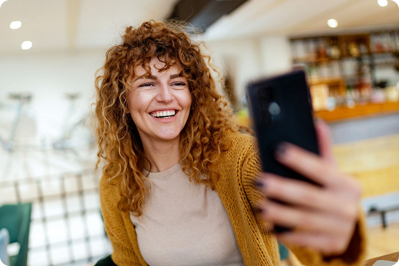 Eine junge Frau schaut lächelnd auf ihr Smartphone
