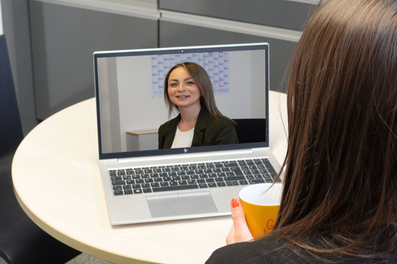 Eine junge Frau mit Kaffeetasse sitzt am Küchentisch vor einem Notebook