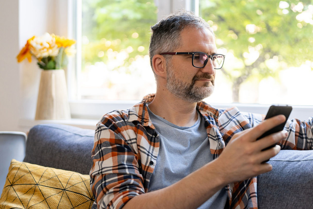 Ein Mann sitzt auf der Couch mit Smartphone und Personalausweis in der Hand