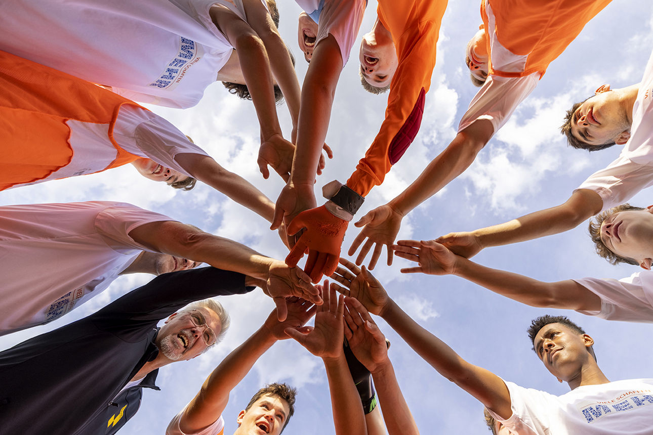 Eine Gruppe von Männern steht im Kreis und hält die Hande sternenförmig zusammen