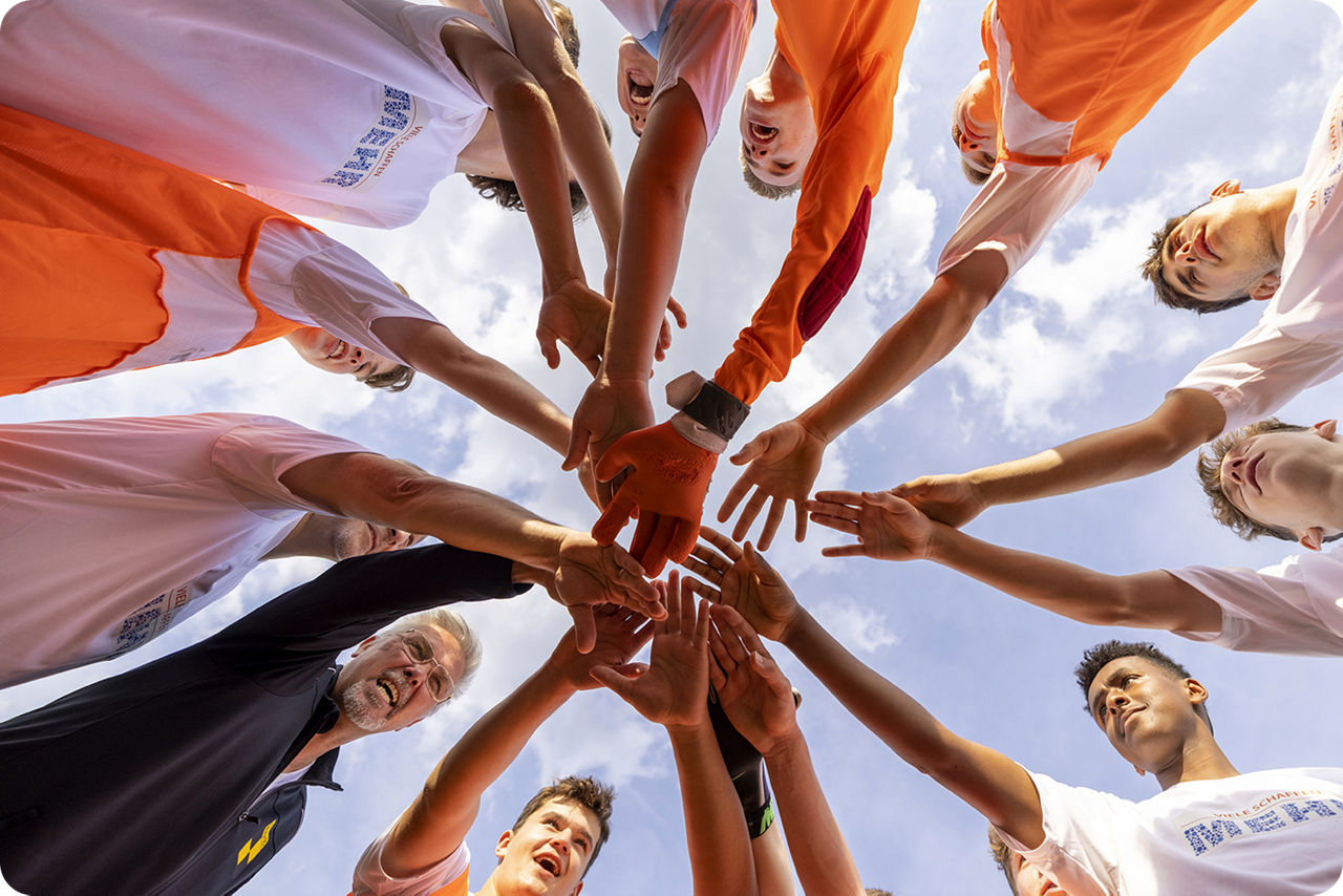 Eine Gruppe von Männern steht im Kreis und hält die Hande sternenförmig zusammen