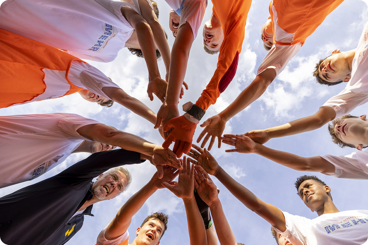Eine Gruppe von Männern steht im Kreis und hält die Hande sternenförmig zusammen