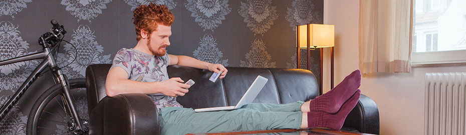 Ein junger Mann hält ein Mobiltelefon und einen Laptop