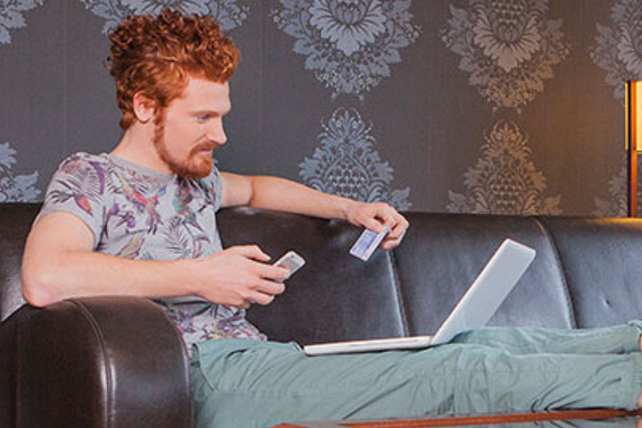 Ein junger Mann hält ein Mobiltelefon und einen Laptop