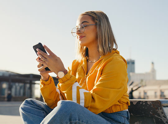 Junge Frau sitzend in gelbem Pullover mit Handy in der Hand
