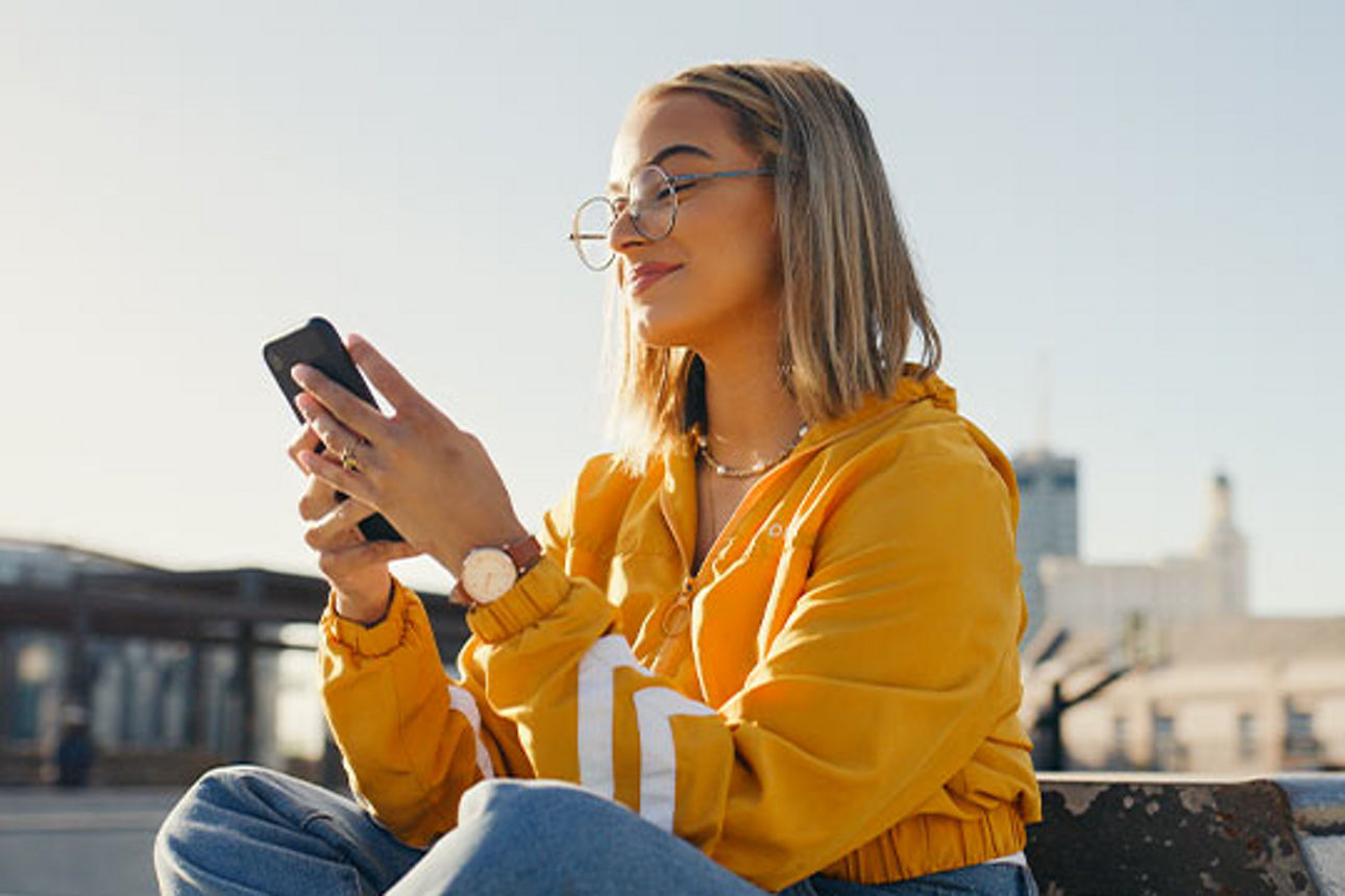 Junge Frau sitzend in gelbem Pullover mit Handy in der Hand