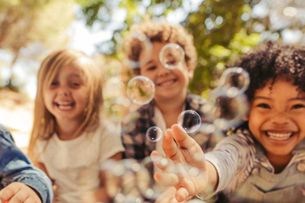 Kinder die mit Seifenblasen im Wald spielen