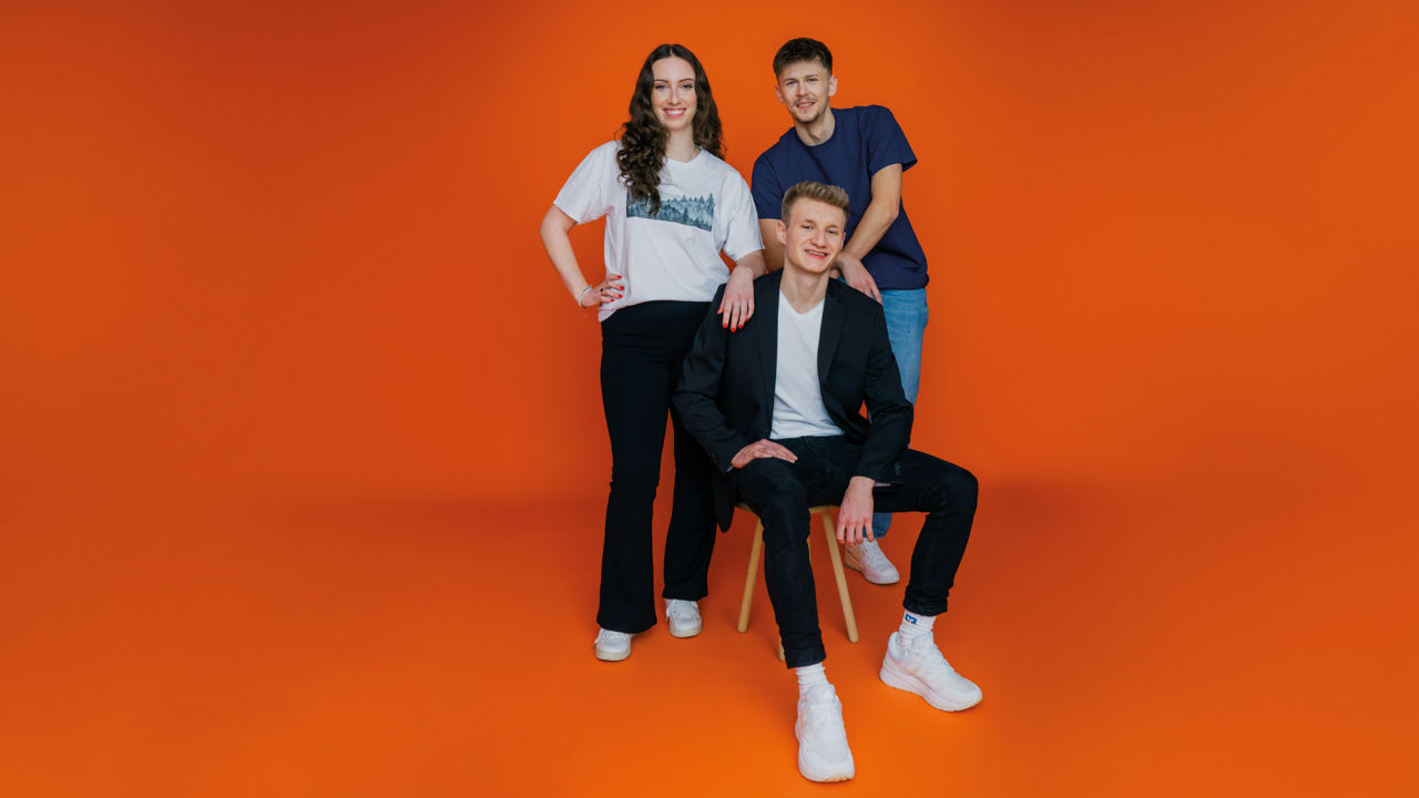 Ein Mädchen und zwei Jungs vor einem orangenen Hintergrund