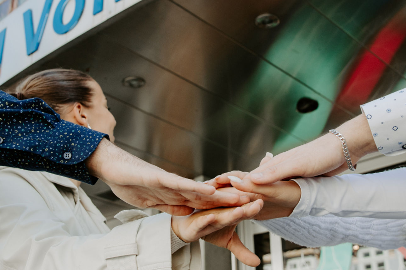Eine Gruppe von Menschen, die ihre Hände in der Mitte zusammenlegen, als Zeichen von Teamarbeit oder Zusammenhalt.