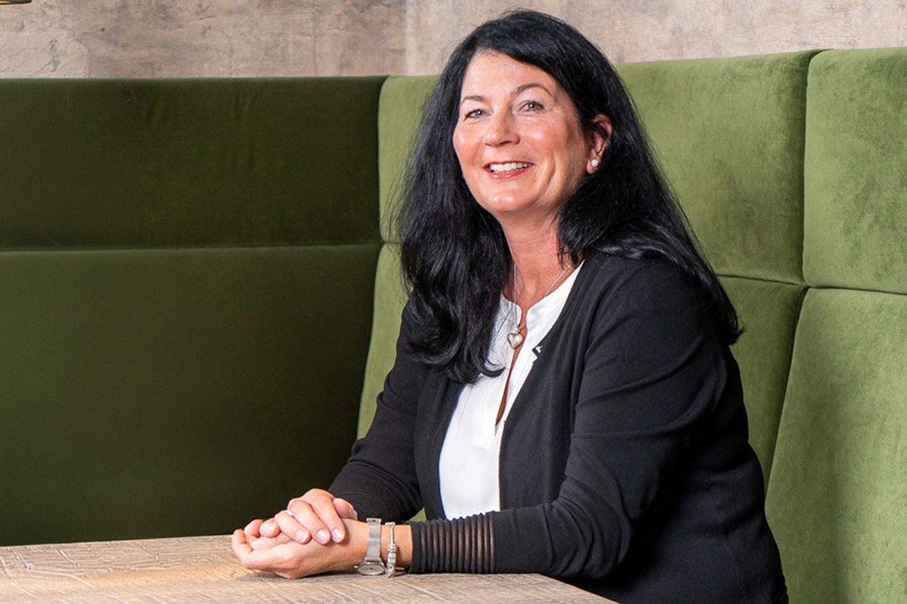 Frau Nelissen der Volksbank Immobilien GmbH sitzt auf einer grünen Sitzbank an einem Tisch