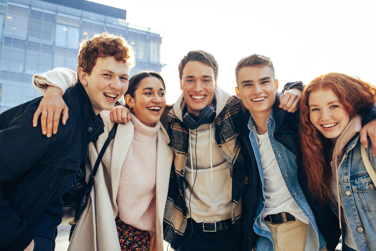 Junge lächelnde Studenten, die sich in die Arme schließen und in die Kamera schauen.