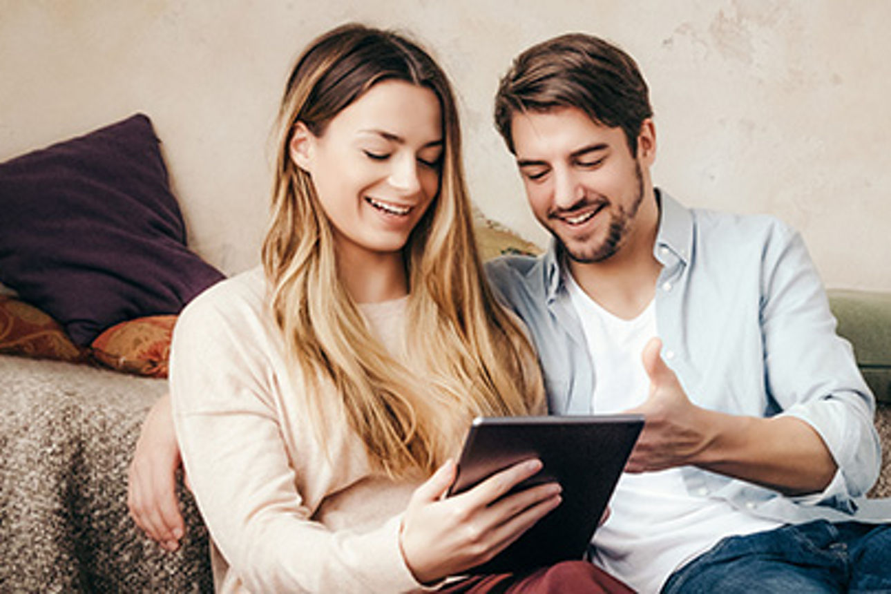 Mann und Frau sitzen im Wohnzimmer am Tablet