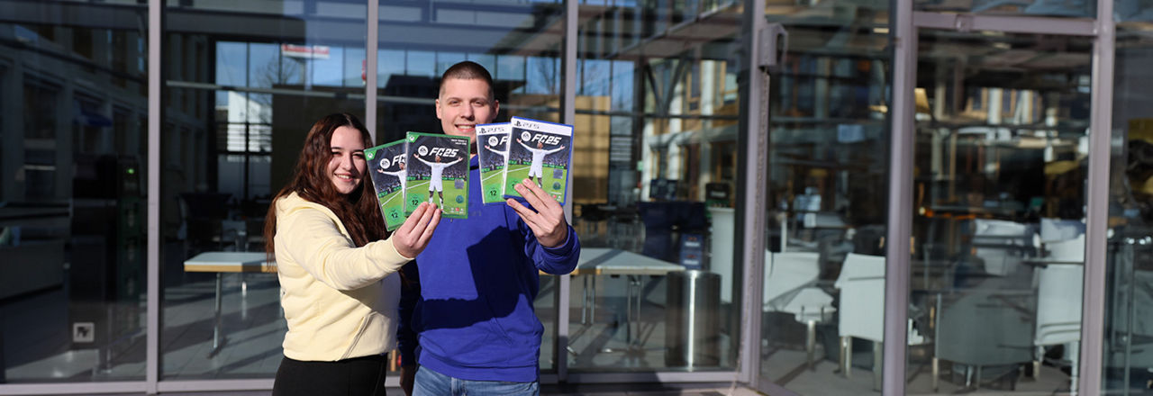 Mann und Frau halten das Gamingspiel FIFA für die XBOX und die Playstation hoch