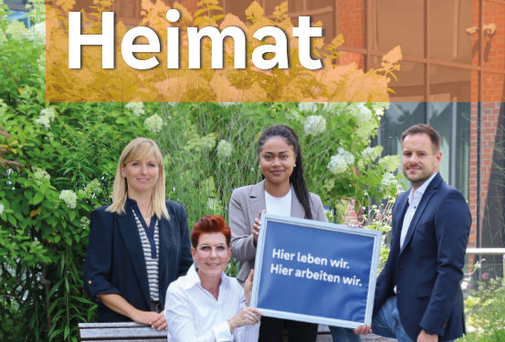 Vier Personen halten ein Schild in der Hand mit der Aufschrift: Hier leben wir. Hier arbeiten wir.