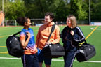 Drei Menschen stehen auf einen Fusballplatz mit der adidas Sporttasche. 