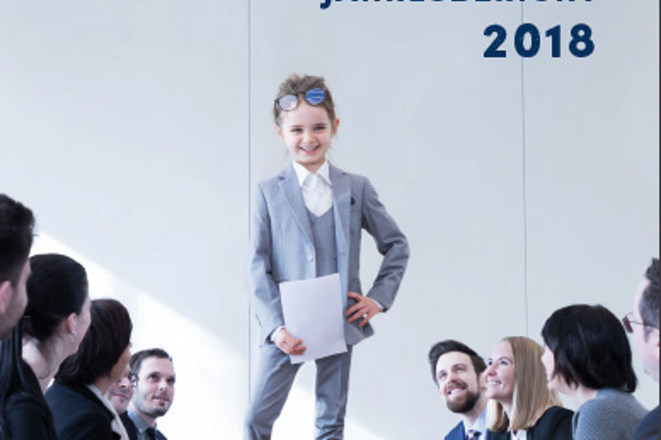 Kind im Anzug steht auf dem Tisch. Drum herum Erwachsene Personen