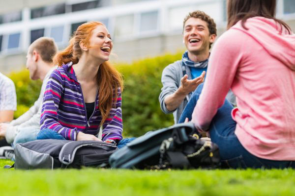Junge Erwachsene sitzen auf der Wiese im Pausenhof