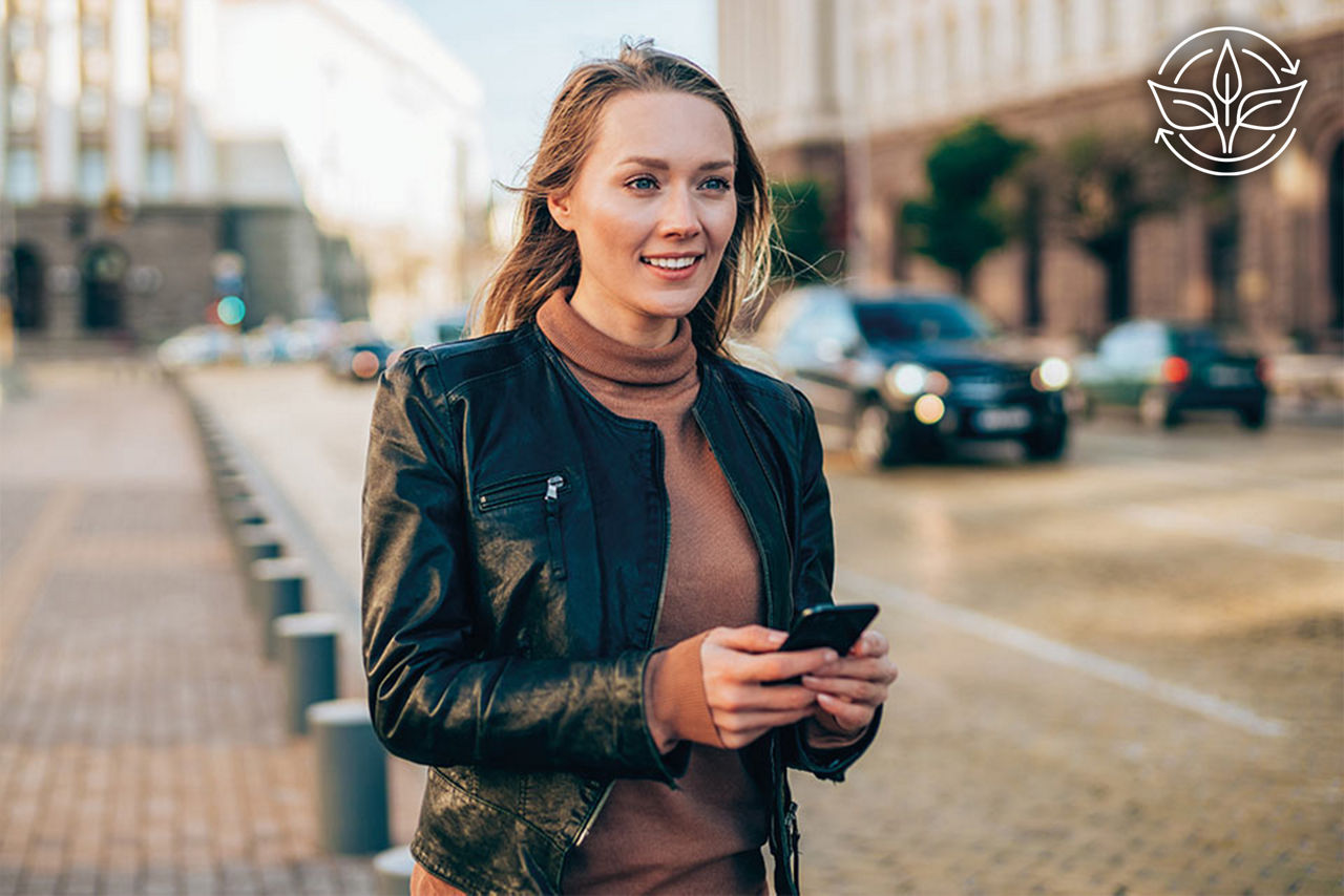 Junge Frau mit Smartphone in der Hand steht auf der Straße und lächelt