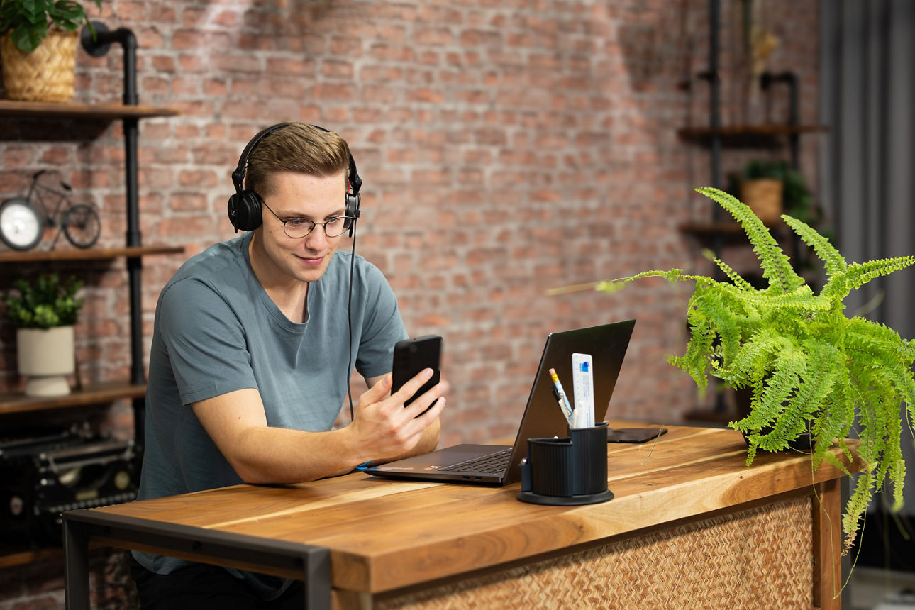 Mädchen lernt am Schreibtisch mit Laptop und Handy in der Hand