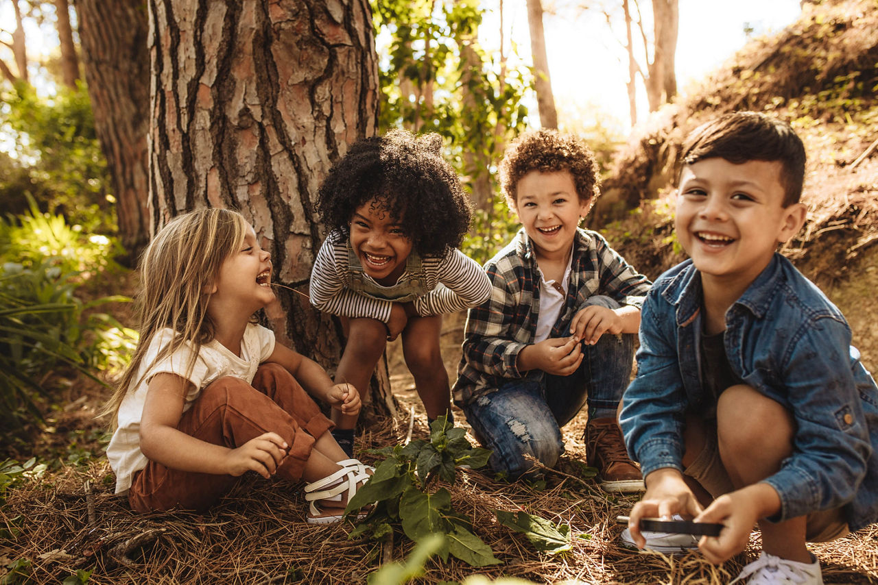 Gruppe an kleinen Kinder spielen zusammen im Wald und schauen in die Kamera