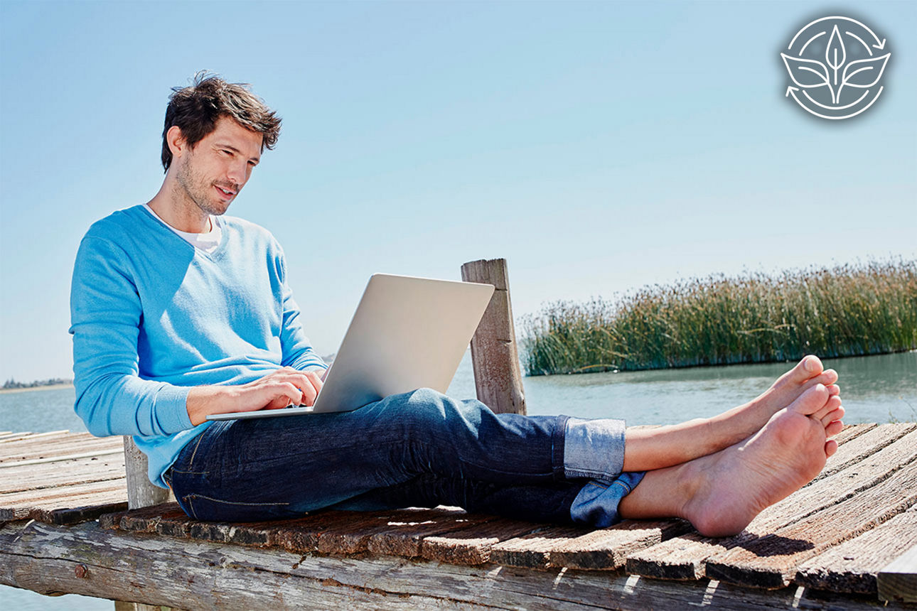 Ein Mann sitzt mit einem Laptop auf dem Schoß auf einem Steg