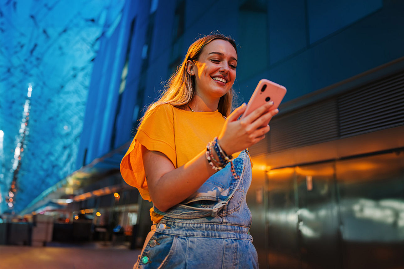 Ein glückliches junges Mädchen nutzt ihr Smartphone, um im Internet zu surfen, während sie nachts auf der Straße unterwegs is