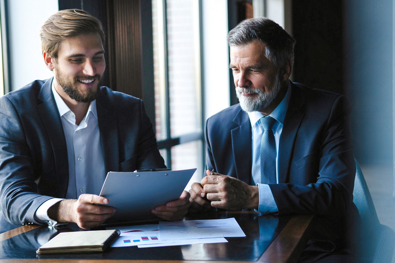 Älterer und jüngerer Geschäftsmann besprechen etwas während ihres Meetings im Büro.