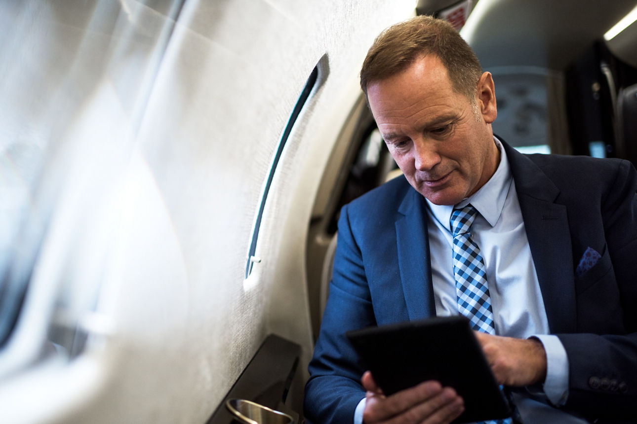 Ein Geschäftsmann sitz im Flugzeug und schaut auf sein Tablet.