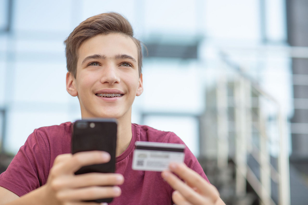 Jugendlicher hält sein Handy und seine Kreditkarte
