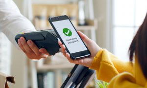Frau bezahlt mit ihrem Handy im Laden an einem mobilen Kartenterminal