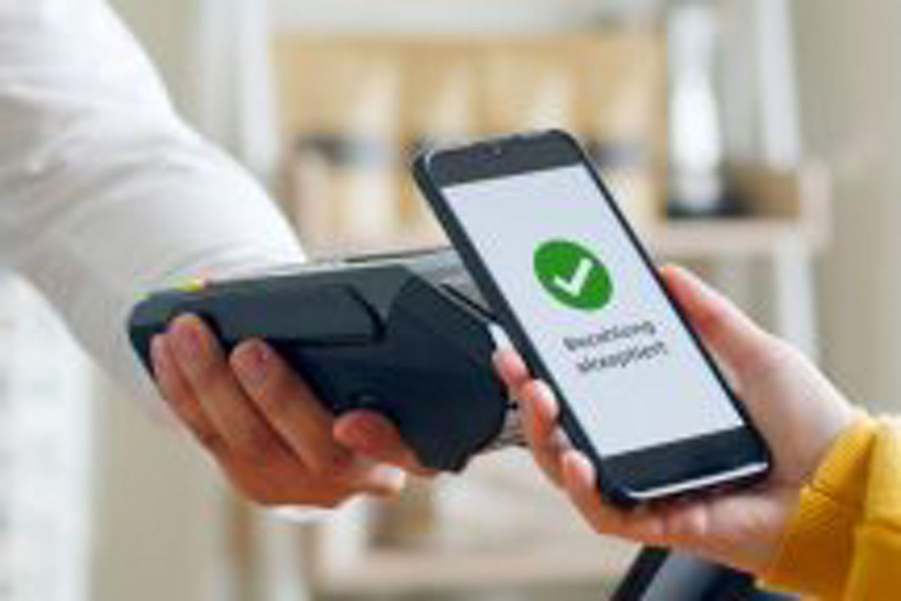 Frau bezahlt mit ihrem Handy im Laden an einem mobilen Kartenterminal